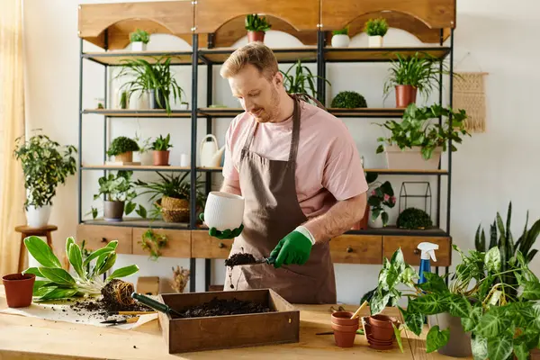 Un hombre en un delantal y guantes riega tiernamente una variedad de plantas exuberantes en una tienda de plantas vibrante. - foto de stock