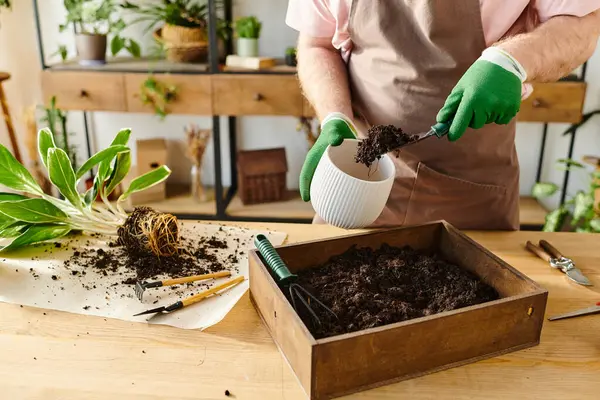 A person in a pink shirt and green gloves carefully placing dirt in a container at a plant shop. — Stock Photo