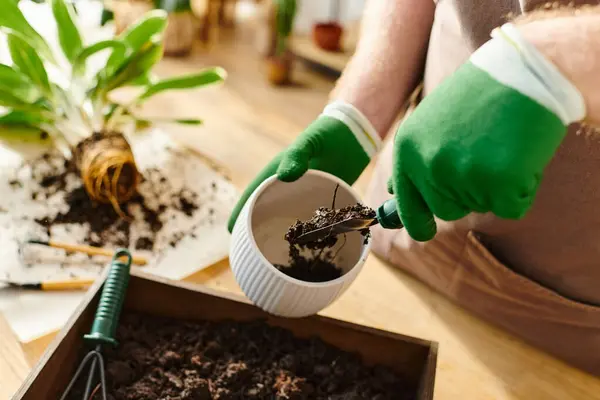 A person in green gloves pouring dirt into a container at a plant shop, embodying the concept of owning a small business. — Stock Photo