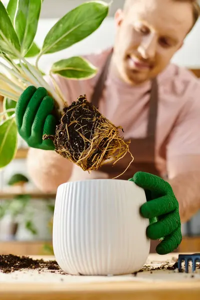 A man delicately holds a potted plant, showcasing its roots with care in a small plant shop, embodying a true connection to nature. — Stock Photo