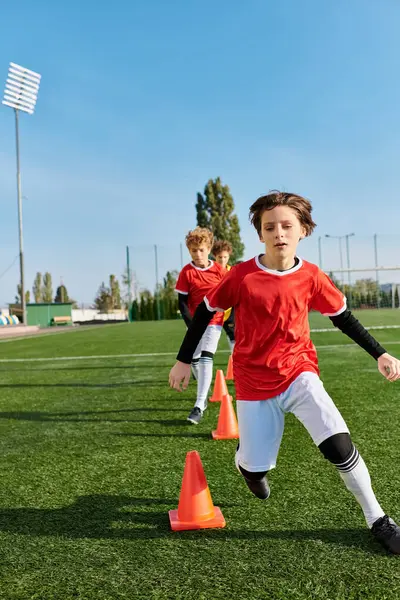 Un giovane ragazzo concentrato prende energicamente a calci un pallone da calcio intorno ai coni, mostrando la sua agilità e precisione nel controllo della palla durante una sessione di prove. — Foto stock