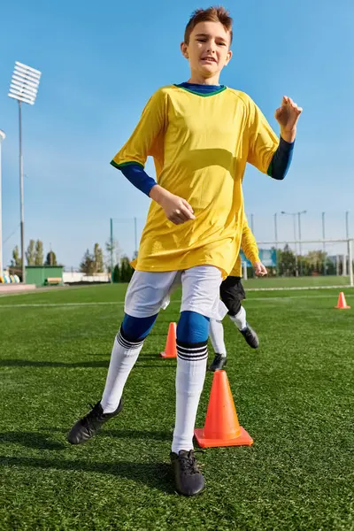 Un niño con uniforme de fútbol patea una pelota de fútbol con determinación y habilidad en un campo verde. - foto de stock