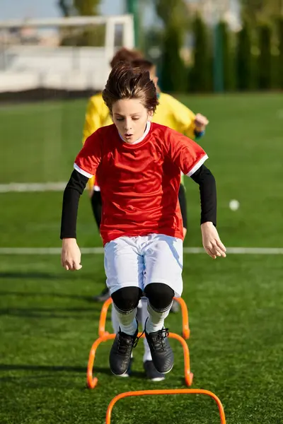 A young boy is energetically kicking a soccer ball across the green soccer field, showcasing his passion and skills in the sport. His concentration and determination are evident as he focuses on perfecting his technique. — Stock Photo