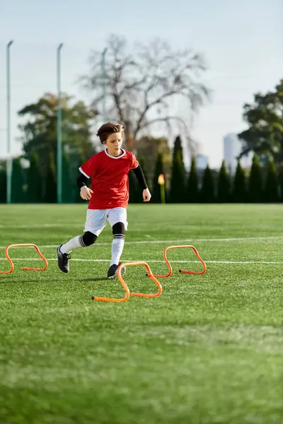 Un jeune garçon frappe habilement un ballon de football sur un vaste terrain, faisant preuve d'agilité et de précision dans ses mouvements.. — Photo de stock