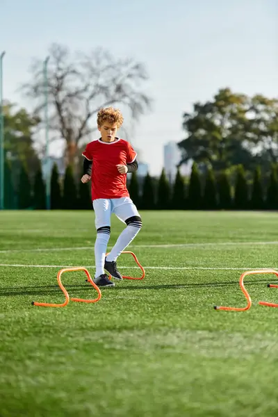 Ein kleiner Junge kickt energisch einen Fußball auf einem Feld und zeigt dabei sein aufkeimendes Talent und seine Leidenschaft für den Sport. Die Sonne scheint hell über ihm, unterstreicht sein entschlossenes Gesicht und das sattgrüne Gras unter seinen Füßen. — Stockfoto
