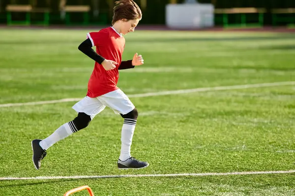 Динамичный молодой мальчик бежит по футбольному полю, сосредоточившись исключительно на предстоящей игре. С решимостью в глазах, он движется быстро и грациозно, демонстрируя свою ловкость и скорость. — стоковое фото