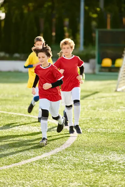 Eine Gruppe kleiner Kinder sprintet voller Energie und Begeisterung über den Fußballplatz, während sie zusammen ein lustiges Spiel spielen.. — Stockfoto