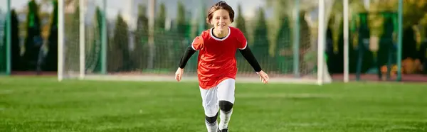 Una joven, vestida con un uniforme de fútbol, corre por el campo de hierba con determinación y rapidez, mostrando su pasión por el deporte. - foto de stock
