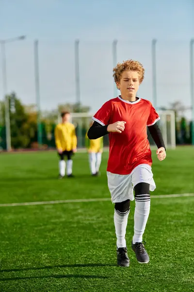 Un niño está corriendo alegremente a través de un campo de fútbol verde exuberante, con el foco en su movimiento ágil y entusiasmo por el juego. - foto de stock