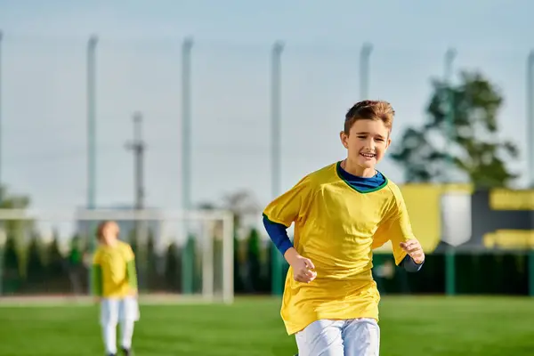 Um menino em uma camisa amarela vibrante se envolve entusiasticamente em um jogo de futebol, chutando habilmente a bola em um campo gramado. — Fotografia de Stock