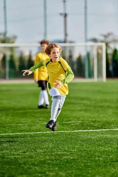 Uma jovem com um uniforme de futebol amarelo e verde está chutando uma bola de futebol com determinação e habilidade. — Fotografia de Stock