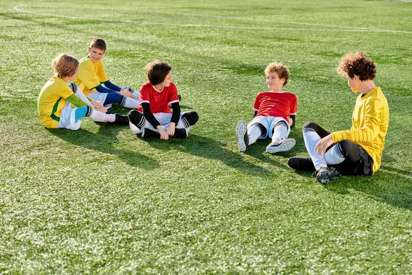 Un vivace gruppo di bambini seduti in cima a un vivace campo verde, crogiolandosi alla calda luce del sole. I loro volti sono pieni di gioia e risate mentre si godono il loro tempo all'aperto. — Foto stock