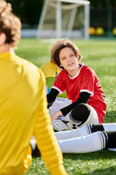 Молодий хлопець сидить на землі поруч з футбольним м'ячем, втраченим у роздумах, коли він розглядає свій наступний хід у грі. — стокове фото