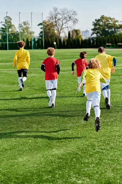 Un animado grupo de niños pequeños jugando con entusiasmo un juego de fútbol en un campo verde, pateando la pelota, corriendo, animando y mostrando el trabajo en equipo y la deportividad. - foto de stock