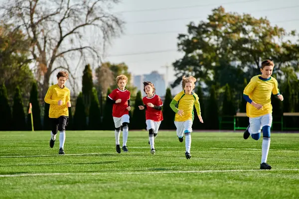 Un grupo de diversos niños pequeños, vestidos con camisetas de colores, juegan al fútbol en un campo empapado de sol, pateando la pelota, corriendo y riendo en camaradería con impaciente determinación. - foto de stock