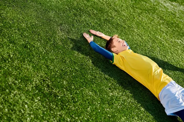 Ein kleiner Junge in Fußballuniform liegt friedlich auf dem Rasen und starrt mit einem Lächeln im Gesicht in den Himmel, verloren in Gedanken an das schöne Spiel. — Stockfoto