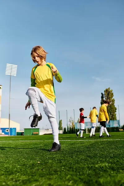 Un niño está pateando apasionadamente una pelota de fútbol en un campo verde. Su expresión enfocada y movimientos hábiles muestran su dedicación y amor por el deporte. - foto de stock