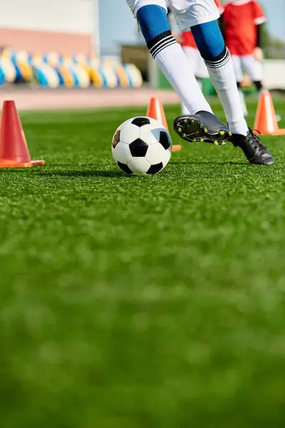Une personne portant des vêtements de sport donne un coup de pied à un ballon de football sur un terrain vert sous un ciel bleu clair par une journée ensoleillée. — Photo de stock