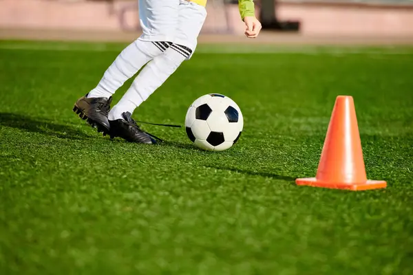 Un ragazzo che mostra abilità calcistiche impressionanti mentre calcia una palla intorno a un cono, mostrando la sua agilità e precisione sul campo. — Foto stock