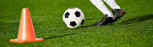 Человек демонстрирует свои футбольные навыки, толкая футбольный мяч вокруг конуса, установленного на поле. Игрок показывает точность и ловкость в маневрировании мячом вокруг препятствия. — стоковое фото