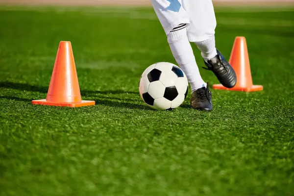 Uma pessoa mostrando habilidades de futebol chutando uma bola em torno de cones de laranja em um campo. O indivíduo é focado e ágil, demonstrando precisão e controle. — Fotografia de Stock