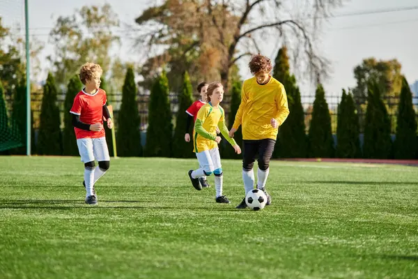 Un groupe animé de jeunes enfants jouant joyeusement à un jeu de football sur un terrain vert. Ils courent, donnent des coups de pied au ballon, et crient avec excitation alors qu'ils s'engagent dans une compétition amicale. — Photo de stock