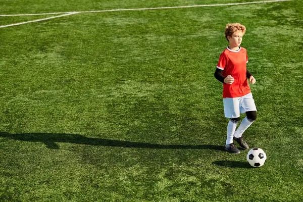 Un ragazzo con una camicia rossa vibrante prende energicamente a calci un pallone da calcio, mostrando la sua passione per lo sport. Il suo sguardo concentrato e il suo atteggiamento deciso mostrano la sua dedizione al gioco.. — Foto stock