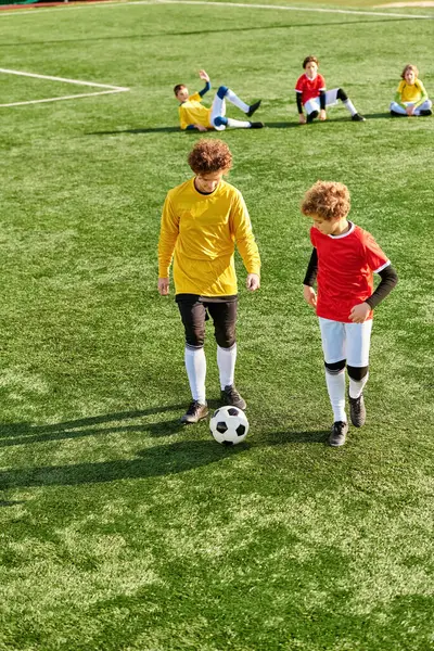 Una escena vibrante de un grupo de niños inmersos en un juego de fútbol en un campo verde. Patean enérgicamente la pelota, corren y se persiguen mutuamente, mostrando el trabajo en equipo y la deportividad. - foto de stock