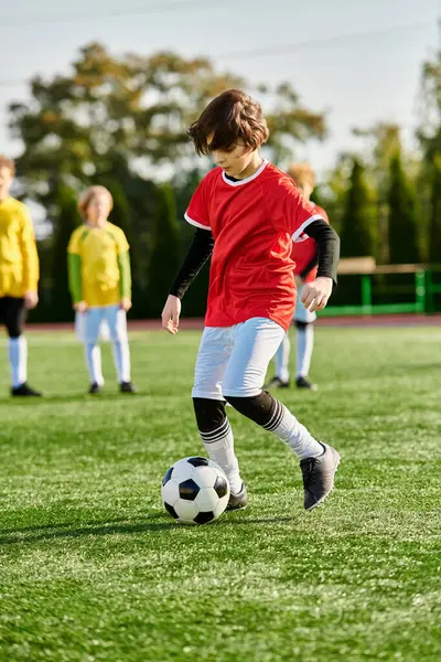 Un niño está pateando una pelota de fútbol en un campo verde, mostrando sus habilidades y pasión por el deporte. El niño está enfocado en la pelota mientras la patea, mostrando agilidad y entusiasmo en sus movimientos. - foto de stock