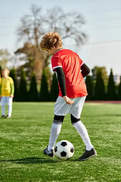 Un ragazzo dall'espressione decisa prende a calci un pallone da calcio su un rigoglioso campo verde sotto il sole splendente, mostrando la sua passione per il gioco. — Foto stock