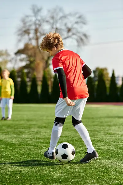 A young boy with a determined expression kicks a soccer ball on a lush green field under the bright sun, displaying his passion for the game. — Stock Photo