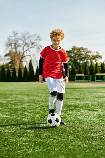 Um menino que mostra suas habilidades de futebol chutando confiantemente uma bola de futebol em um campo gramado. Seu foco e determinação brilham enquanto ele pratica sua técnica em campo. — Fotografia de Stock
