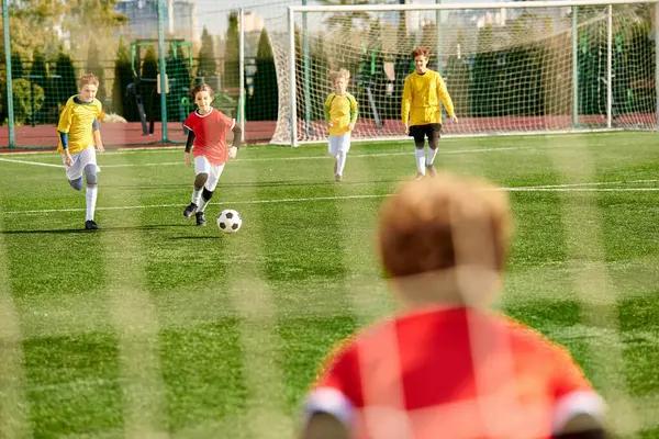 Un groupe de jeunes enfants dynamiques jouant avec enthousiasme à un jeu de football, courant, donnant des coups de pied au ballon, et s'acclamant mutuellement d'une manière vivante et animée. — Photo de stock