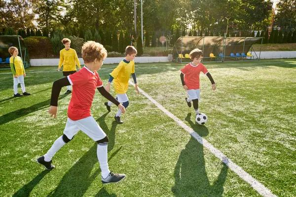 Un groupe de jeunes garçons jouant avec enthousiasme un jeu de football sur un terrain vert. Ils courent, donnent des coups de pied au ballon, s'encouragent mutuellement, font preuve de travail d'équipe et d'esprit sportif. — Photo de stock