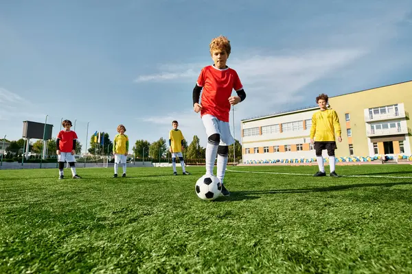 Une scène dynamique se déroule alors qu'un groupe de jeunes garçons donne un coup de pied énergique autour d'un ballon de football, mettant en valeur leurs compétences et leur travail d'équipe sur le terrain. — Photo de stock