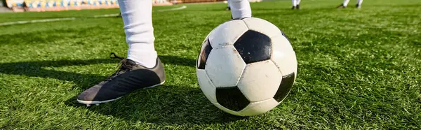 Une personne debout au sommet d'un ballon de football sur un terrain vert luxuriant, mettant en valeur l'équilibre parfait et l'habileté dans un exploit athlétique magnifique. — Photo de stock