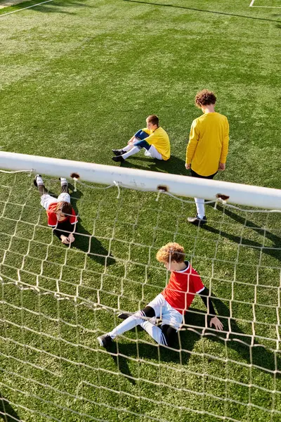 Un grupo de jóvenes se sientan triunfalmente en la cima de un campo de fútbol, disfrutando de un merecido descanso después de un partido. Están charlando, riendo, y celebrando su victoria. - foto de stock