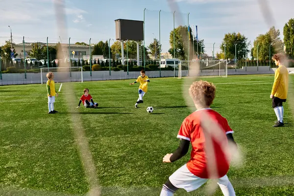 Un groupe de jeunes enfants jouent à un jeu énergique de football sur un terrain herbeux. Ils courent, passent et donnent des coups de pied au ballon avec excitation et travail d'équipe. Les enfants rient et applaudissent alors qu'ils s'engagent dans une compétition amicale. — Photo de stock