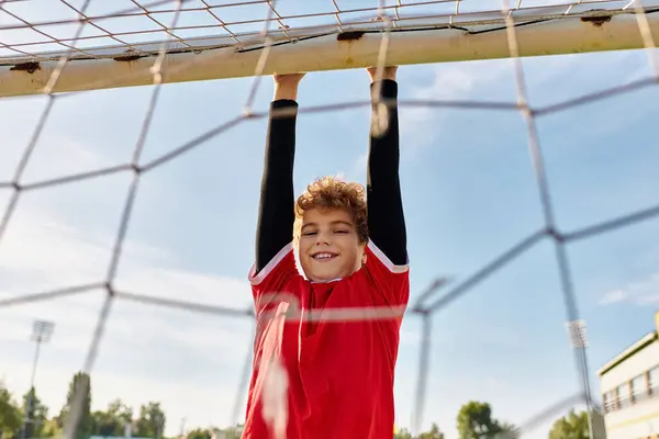 Un giovane ragazzo di talento in una vibrante camicia rossa gioca con entusiasmo a calcio, calci la palla con precisione e abilità su un campo di erba verde. — Foto stock