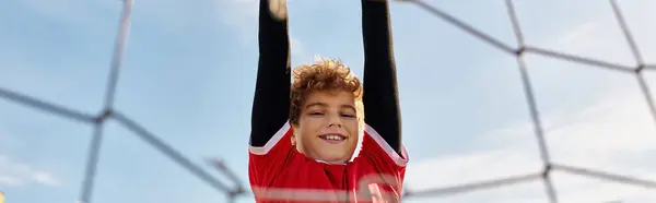 Грайливий молодий хлопчик висить догори ногами в барвистій волейбольній сітці, демонструючи свій пригодницький дух і любов до унікальних занять. — стокове фото