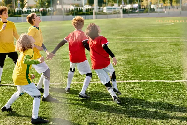 Un groupe de jeunes enfants jouent joyeusement à un jeu de football sur un terrain herbeux. Ils courent, donnent des coups de pied au ballon, s'encouragent mutuellement, font preuve de travail d'équipe et d'esprit sportif. — Photo de stock
