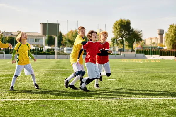 Una vibrante escena se desarrolla mientras un grupo de enérgicos niños pequeños participan en un juego de fútbol en un campo de hierba. Vestidos con camisetas de colores, driblan, pasan y disparan la pelota con entusiasmo, mostrando el trabajo en equipo y la deportividad.. - foto de stock