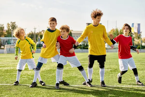 Група молодих хлопчиків гордо стоїть на футбольному полі, демонструючи єдність і рішучість. Вони купаються в теплому сяйві заходу сонця, з яскраво-зеленим полем, що простягається під ними. — стокове фото