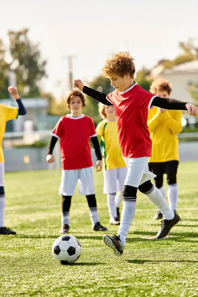 Un grupo de niños jugando al fútbol enérgicamente en un campo verde vibrante, pateando la pelota, corriendo, riéndose y animándose unos a otros bajo el sol brillante. - foto de stock