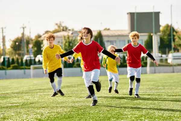 Un animado grupo de jóvenes con caras brillantes participan en un intenso juego de fútbol en un campo soleado. Los chicos están corriendo, pateando y pasando la pelota con entusiasmo, mostrando sus habilidades y trabajo en equipo. - foto de stock
