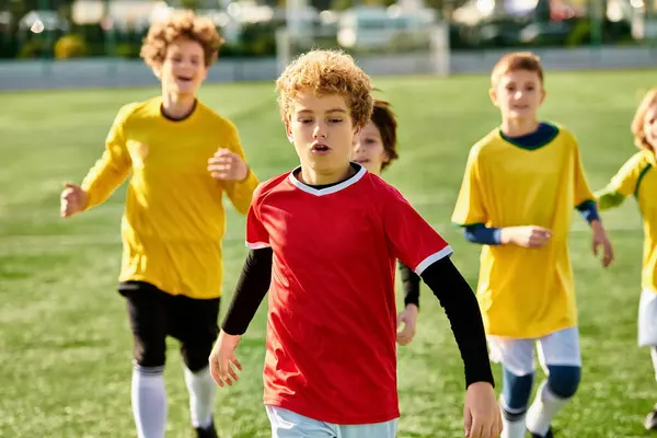 Un grupo de jóvenes enérgicos que participan en un partido amistoso de fútbol, correr, patear y pasar la pelota en un campo soleado. - foto de stock