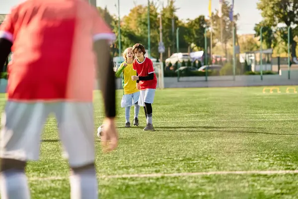 A spirited group of young people engaged in a competitive game of soccer on a grassy field, displaying teamwork, speed, and skill as they kick the ball towards the goal amidst cheers and laughter. — Stock Photo