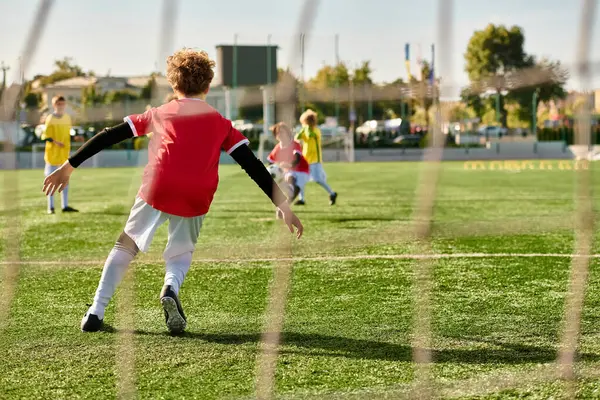 Um grupo de crianças pequenas, cheio de emoção e energia, se envolver em um jogo amigável de futebol. Eles correm, chutam e perseguem a bola com entusiasmo em um campo verde sob o sol brilhante. — Fotografia de Stock