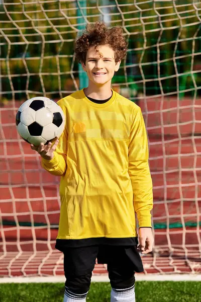 Un joven se para frente a un gol, sosteniendo una pelota de fútbol en sus manos, listo para disparar, con determinación en sus ojos. - foto de stock
