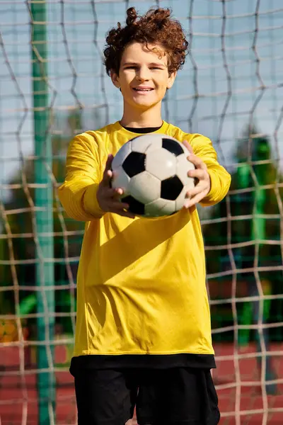 Un joven se para frente a una red, sosteniendo una pelota de fútbol en sus manos, listo para disparar. Él está enfocado y decidido, con el objetivo en su mira. - foto de stock